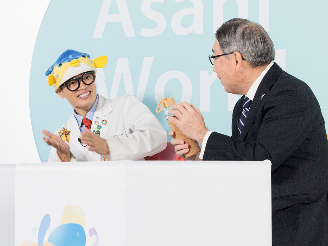 さかなクン（左）に、再生可能なガラス製のマイボトルを紹介する島村理事長（右）