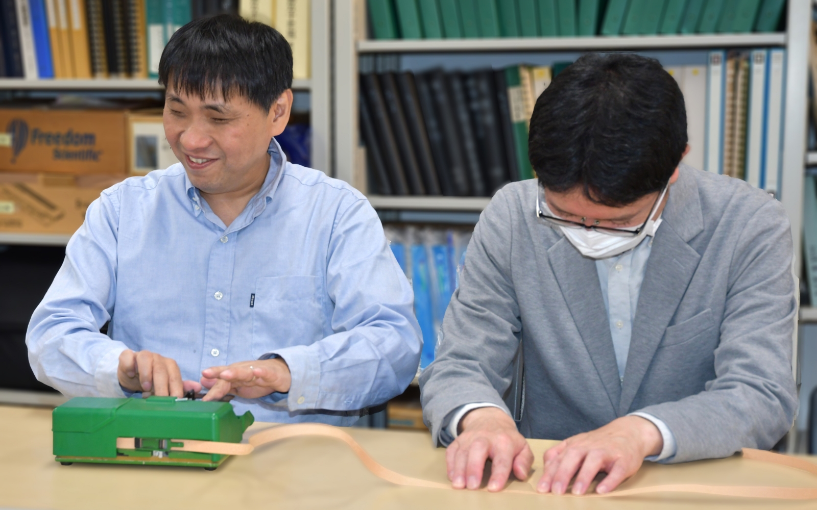 ブリスタを打つ大河内直之さんと点字テープを読む人の写真