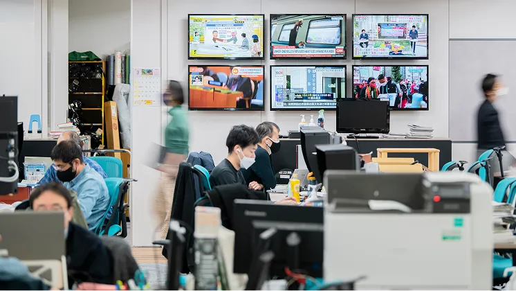 複数のモニターが壁に設置されたオフィスで、社員がパソコンに向かい仕事をしている様子