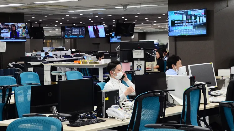 オフィスで複数の社員がパソコンを操作したり携帯電話で話したりしながら業務を行っている様子